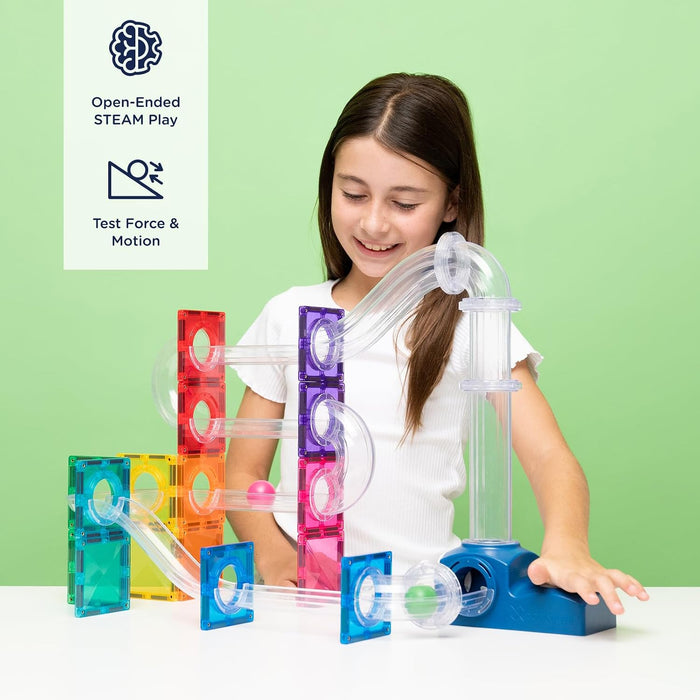 A girl playing with a colorful magnetic tile ball run featuring clear tubes, rainbow tiles, and a blue launcher.