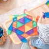 Child playing with colorful rainbow magnetic equilateral and isosceles triangle tiles on a light-colored floor.
