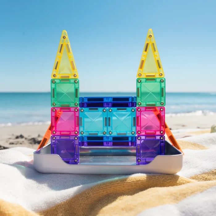 Vibrant translucent magnetic squares and triangles built into a castle on a metal tray at a sunny beach.
