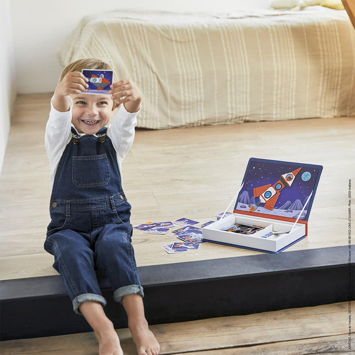Child playing with a blue book-shaped magnetic puzzle box featuring rockets and planets in a cosmic space scene.