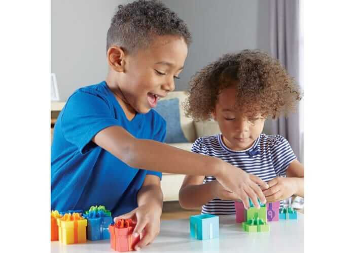 Boy and girl playing with colorful plastic gift boxes featuring bows and numbers on a table.