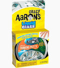 Yellow box showing a round tin of clear, glass-like putty with a hand visible through the transparent material.