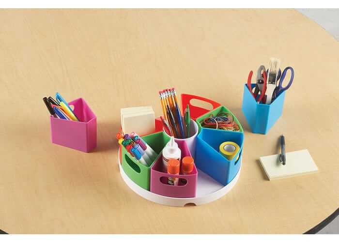 Colorful wedge containers on a white rotating base filled with art supplies on a light wood table.