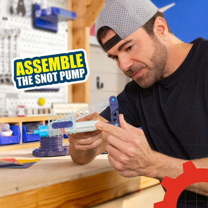 Mark Rober builds a blue and white plastic snot pump toy. Overlay text reads: Assemble the Snot Pump.