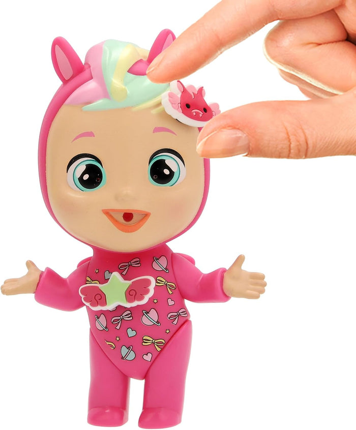 Pink mini doll with pastel hair and teal eyes. A hand places a winged dragon charm on its forehead.