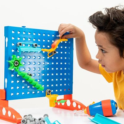 Child building a marble run on a blue pegboard using colorful plastic pieces, screws, and a toy power drill.