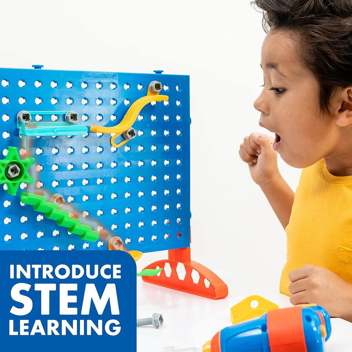 Excited boy watches marble on blue pegboard maze with colorful tracks and gears. STEM learning text and toy drill.