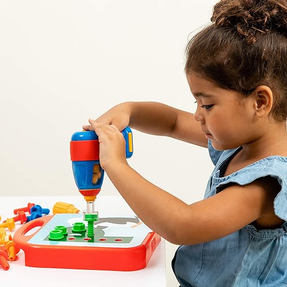 Girl uses a blue and red toy drill to screw a green bolt into a pegboard on a red base with colorful plastic bolts.
