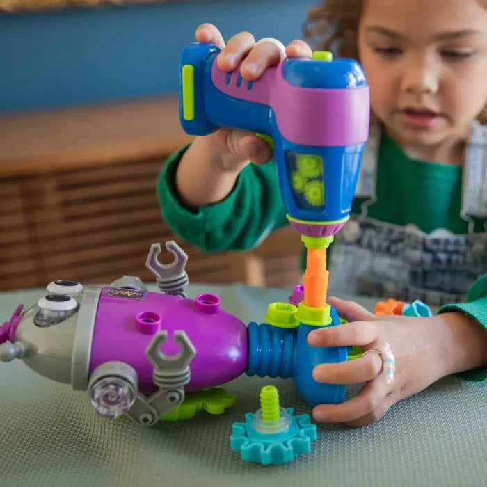 Child using a purple and blue toy power drill to assemble a purple robot with lime green parts and gears.