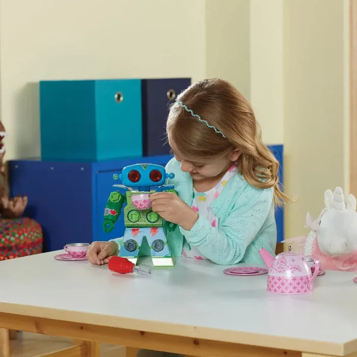 Girl plays with a blue and green floral robot with bolt details, using a red toy screwdriver and a pink tea set.