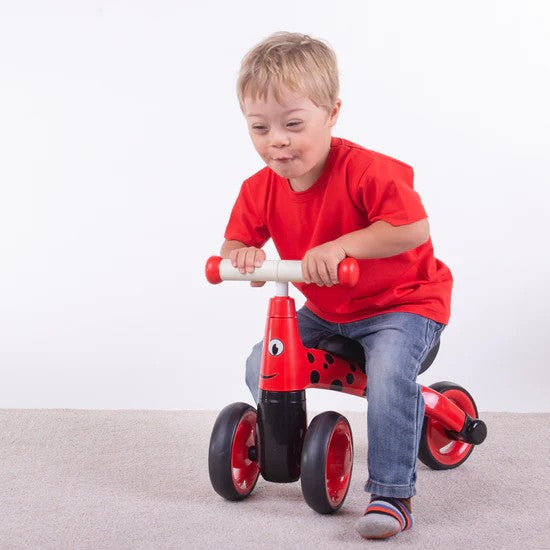 Child riding a red ladybird-themed trike with black spots and white handlebars against a white background.