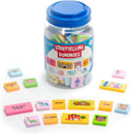 Clear jar with blue lid and colorful tiles featuring story words and pictures scattered on a white surface.