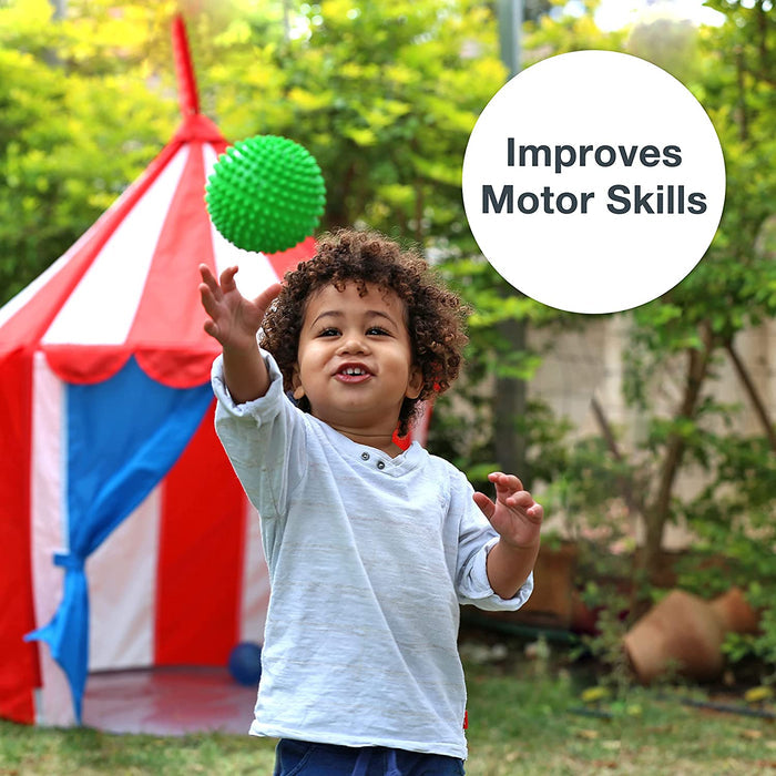 Child reaching for a green nubby sensory ball in the air with a red and white play tent in the background.