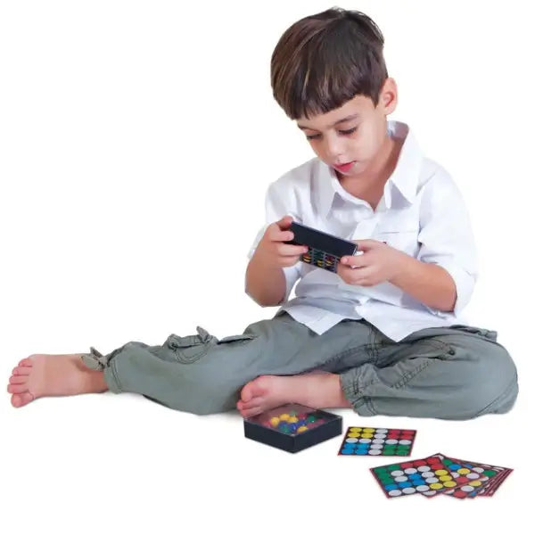 Child manipulating colored marbles in a black puzzle tray to match patterns shown on small cards.