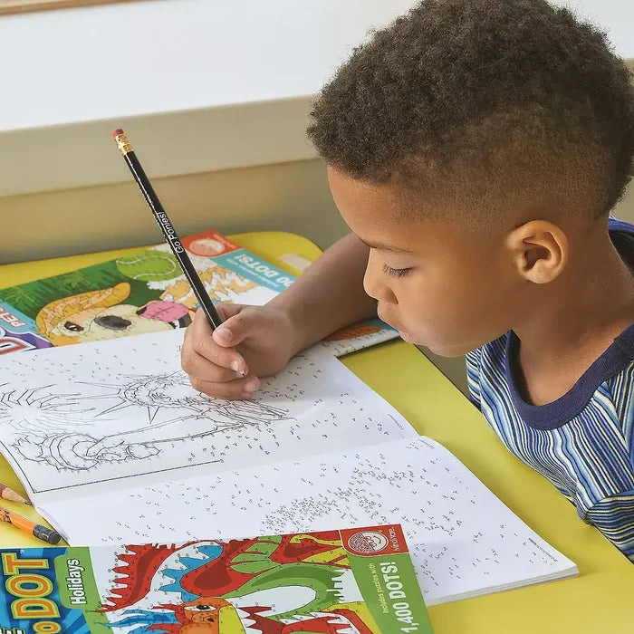 A boy connects numbered dots in an Extreme Dot to Dot activity book with intricate patterns and colorful animal art.