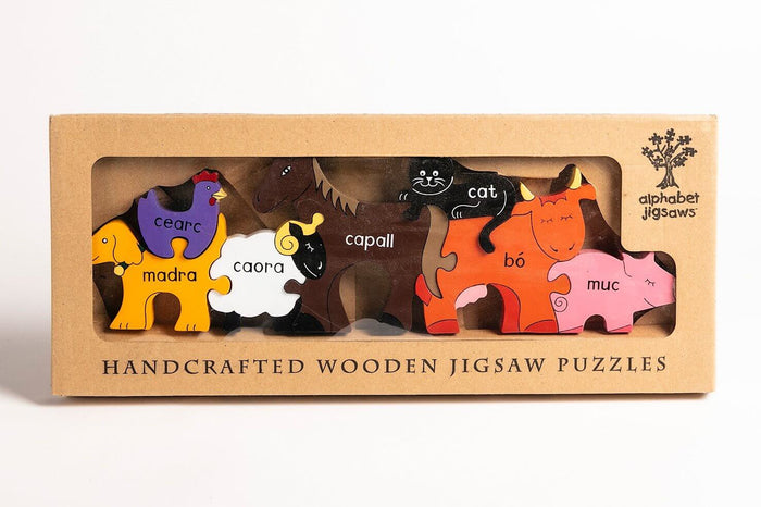 Handcrafted wooden puzzle with colorful farm animals labeled in Irish, shown inside a cardboard window box.