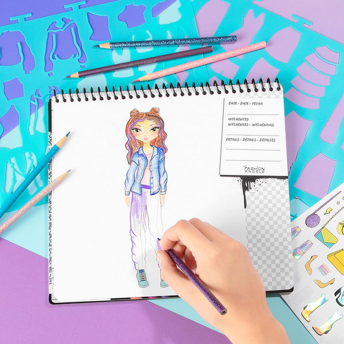 Hand coloring a fashion sketch in a spiral notebook with glittery pencils, teal stencils, and stickers.