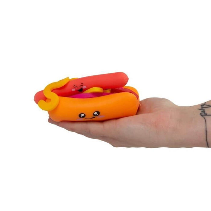 Hand holding an orange and red squishy hot dog toy with cute smiling faces and a yellow mustard zigzag.