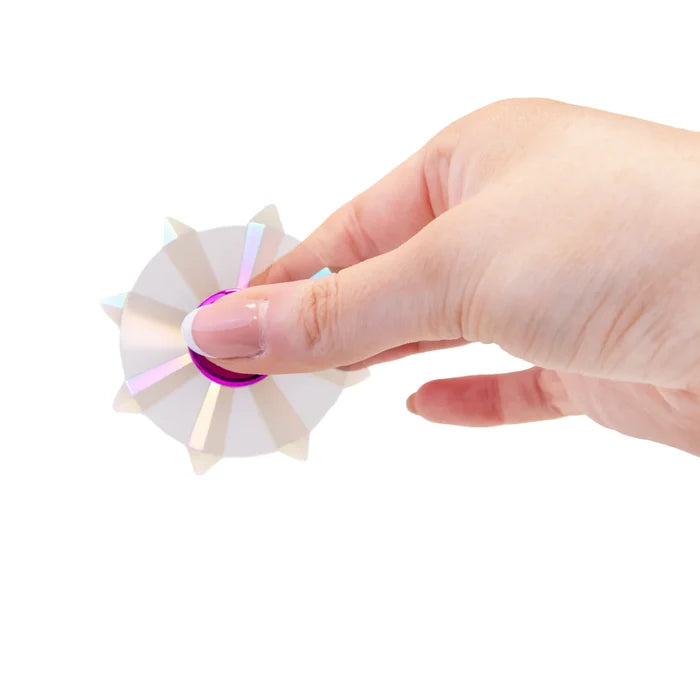 Hand holding an iridescent spiked fidget spinner with a purple center hub against a white background.