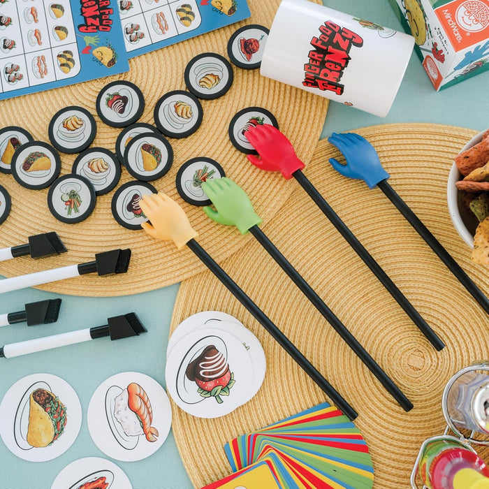 Four colorful plastic hand grabbers reaching for circular food tokens on woven placemats.