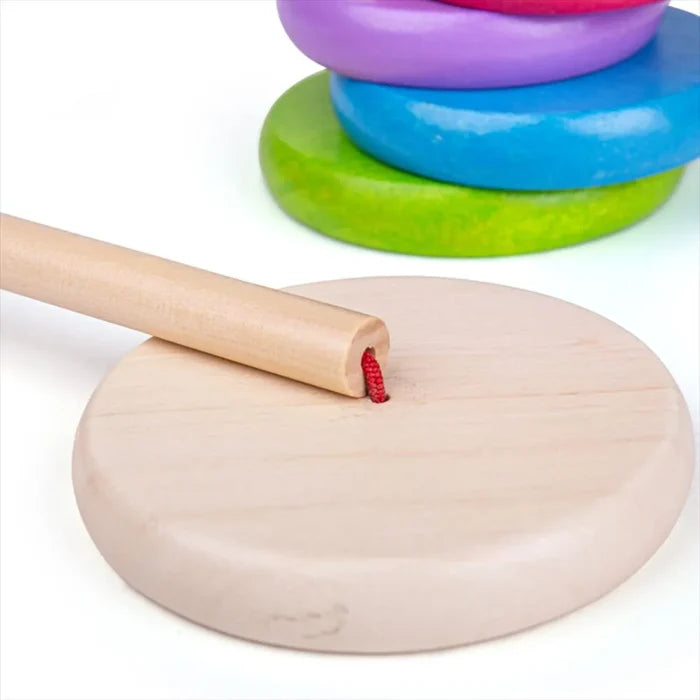 Circular wood base and pole with red cord, with rounded purple, blue, and green stacking rings in the background.
