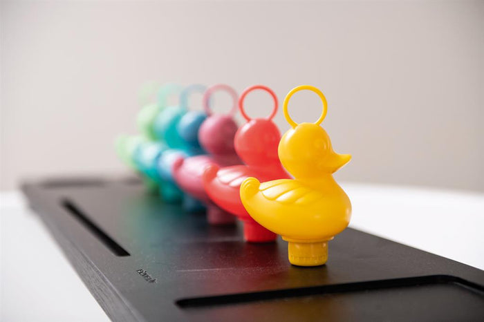 A row of rainbow-colored plastic ducks with fishing rings on their heads, ranging from yellow to green.