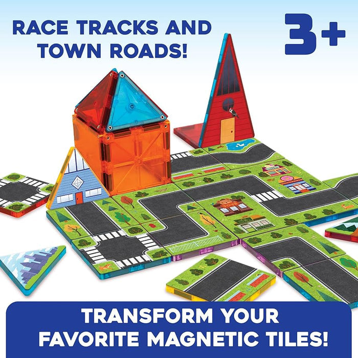 Road-patterned magnetic tiles with grass and trees used to build a toy town with colorful translucent buildings.