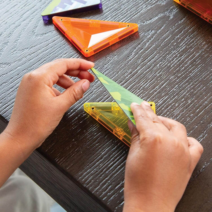 Hands placing a green patterned triangle over a translucent yellow magnetic tile on a dark wood table.