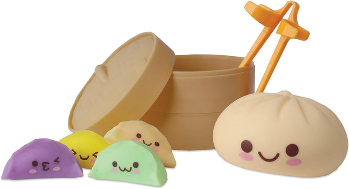 Tan plastic steamer with lid, orange tongs, large cream bun, and four colorful mini dumplings with cute faces.