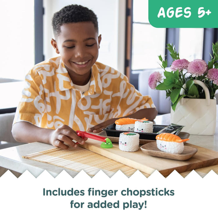 Smiling boy plays with a toy sushi set featuring cute-faced sushi pieces, red finger chopsticks, and wasabi.