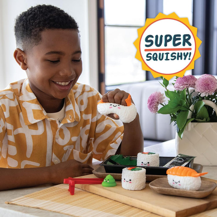 Smiling boy squeezes a sushi squishy toy. Includes various sushi-shaped fidgets with faces on a wooden board.