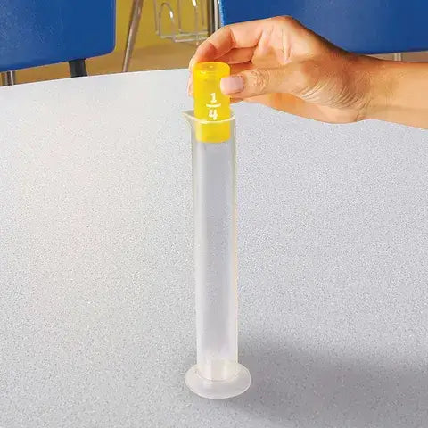 Hand drops a small yellow cylinder labeled 1/4 into a tall clear tube on a grey tabletop.
