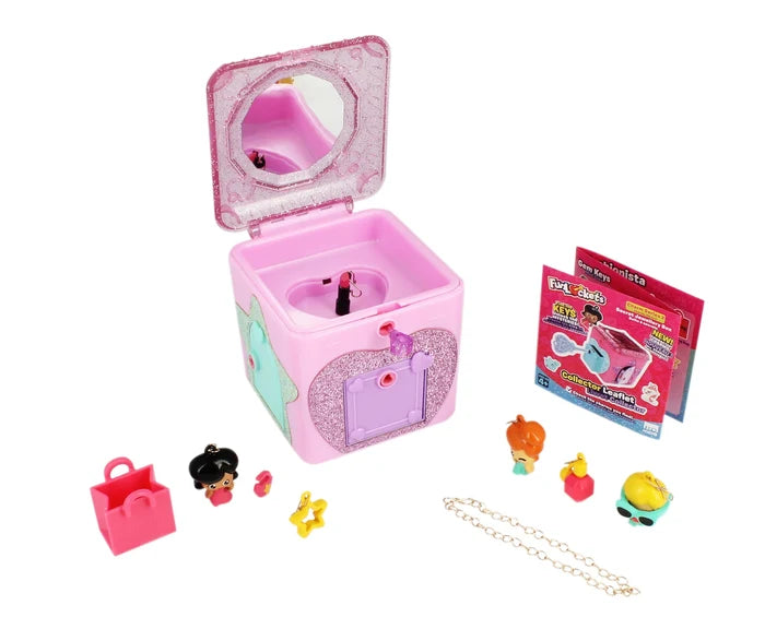 Open pink glittery toy jewelry box with mirror, various colorful charms, a gold chain, and a collector leaflet.