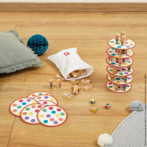 Tower of colorful dotted discs and wooden character blocks with a white cloth bag and dice on a light wood floor.
