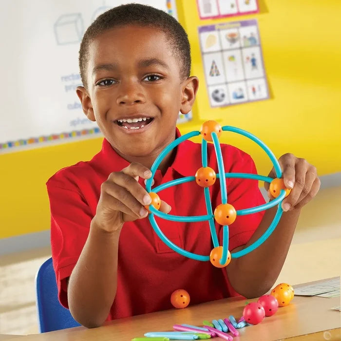 A child holds a sphere made of teal curved rods and orange connectors from a colorful geometric building set.