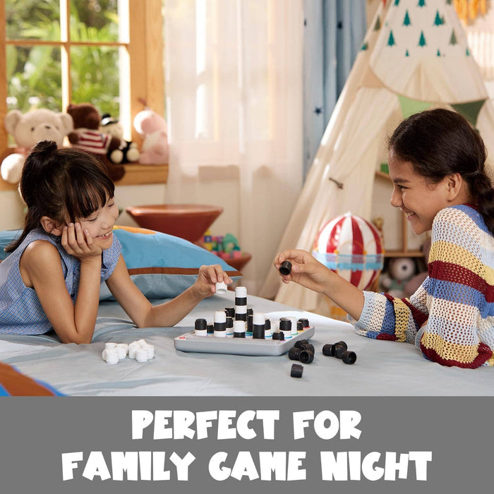 Two girls play a 3D board game with black and white cylindrical pieces on a gray electronic base on a bed.