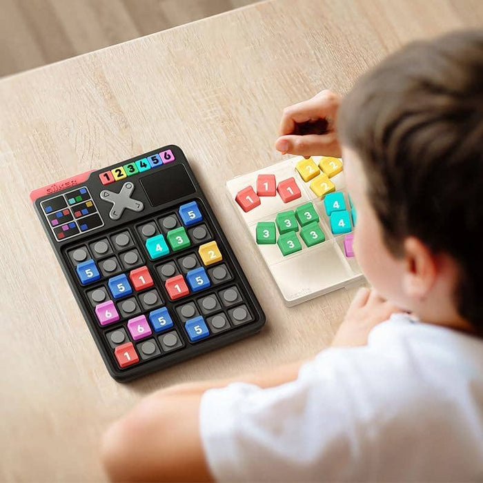 Child playing with a black handheld electronic grid game and colorful numbered tiles on a wooden table.