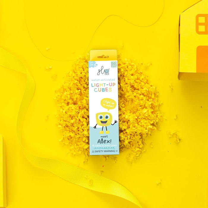 Yellow Glo Pals Alex packaging centered on yellow shredded paper and ribbon against a bright yellow background.