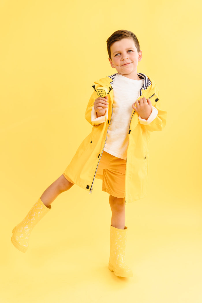 Boy in a yellow raincoat holds a yellow cube toy with a winking smiley face.