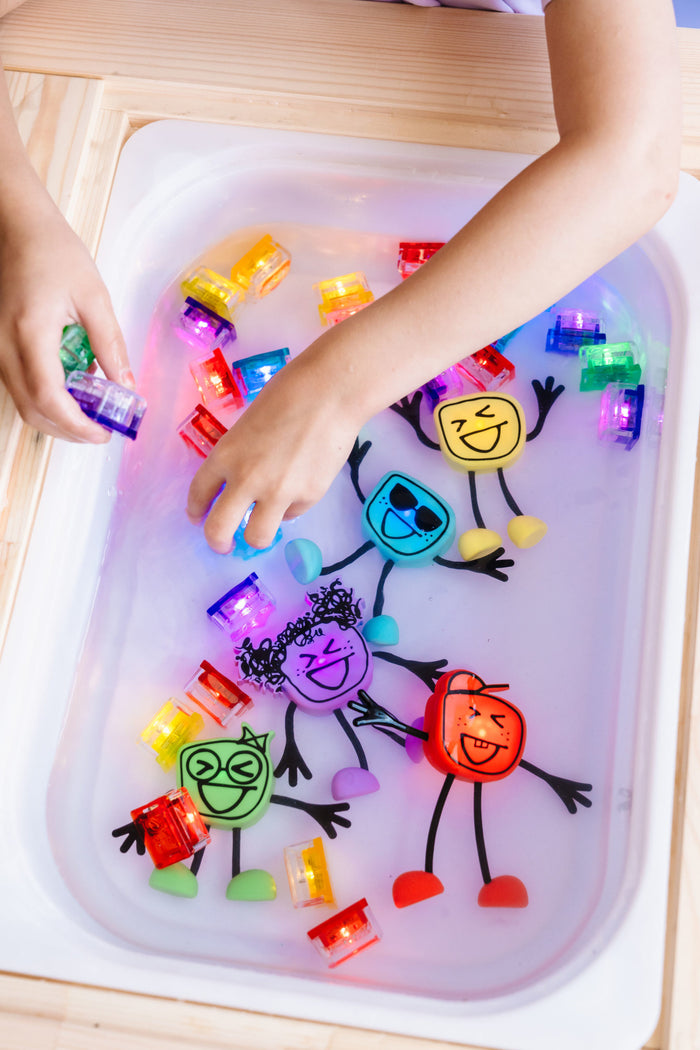 Child's hands reach for colorful, light-up cubes in water alongside illustrated cartoon character figures.