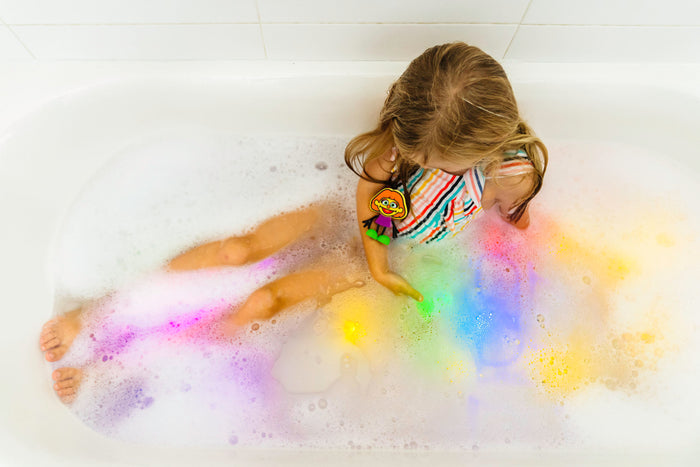 Child in a bubble bath with vibrant pink, yellow, and blue light-up cubes glowing through bubbles underwater.