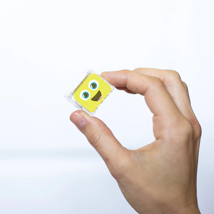 Hand holding a small, clear square cube with a yellow smiling cartoon face against a white background.