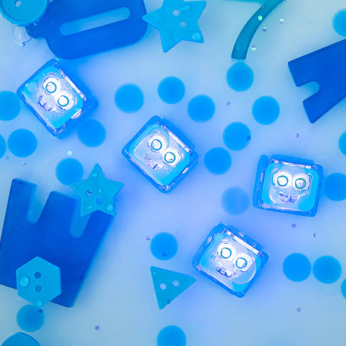 Four blue light-up cubes with happy faces submerged in blue water with various blue plastic stars and shapes.