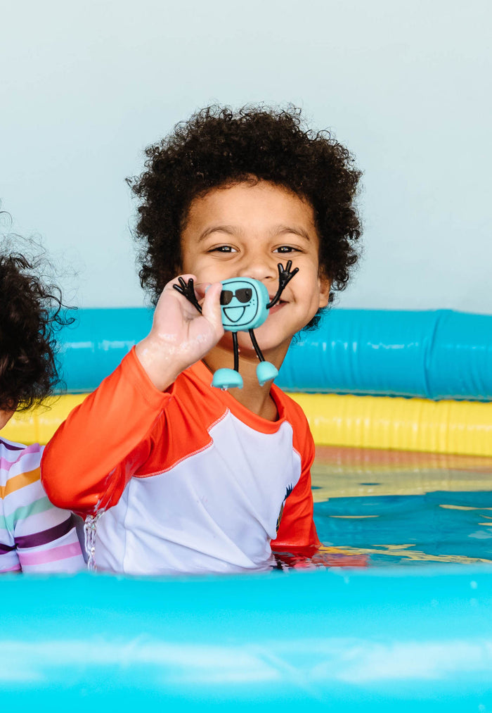 Child in a pool holding a light blue cube-shaped character toy with black sunglasses and spindly limbs.