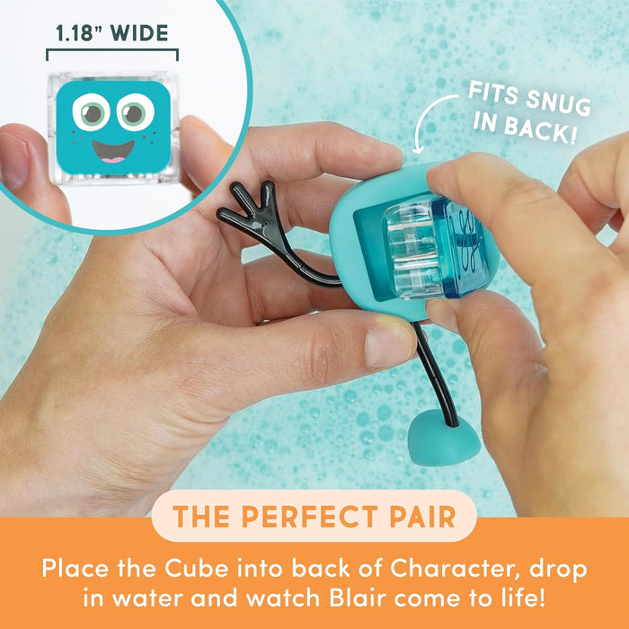 Hands insert a square blue light-up cube into the back of a teal Blair character toy over bubbly bath water.
