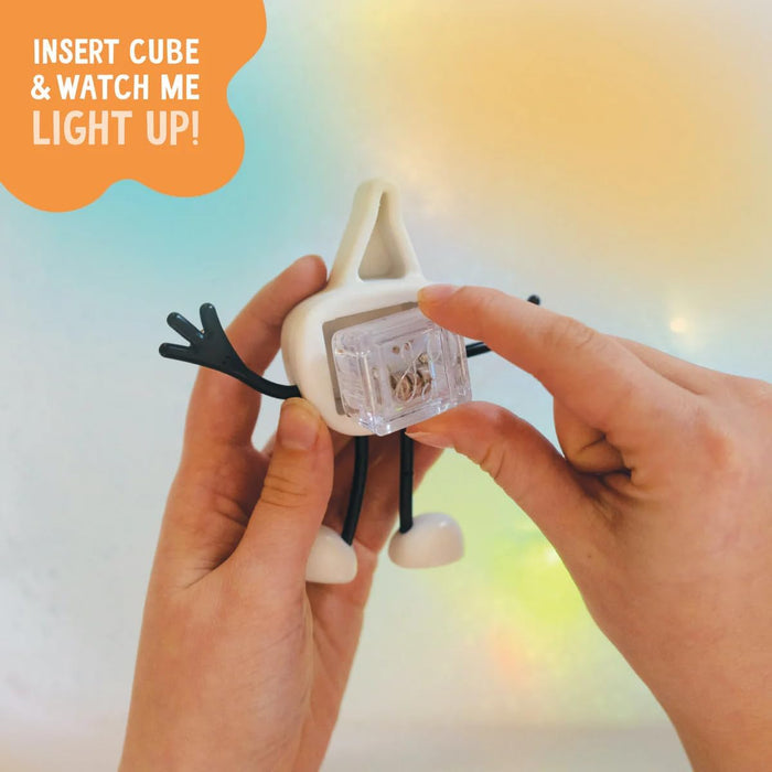 Hands insert a clear cube into a white character with black arms. Orange bubble: Insert cube & watch me light up!
