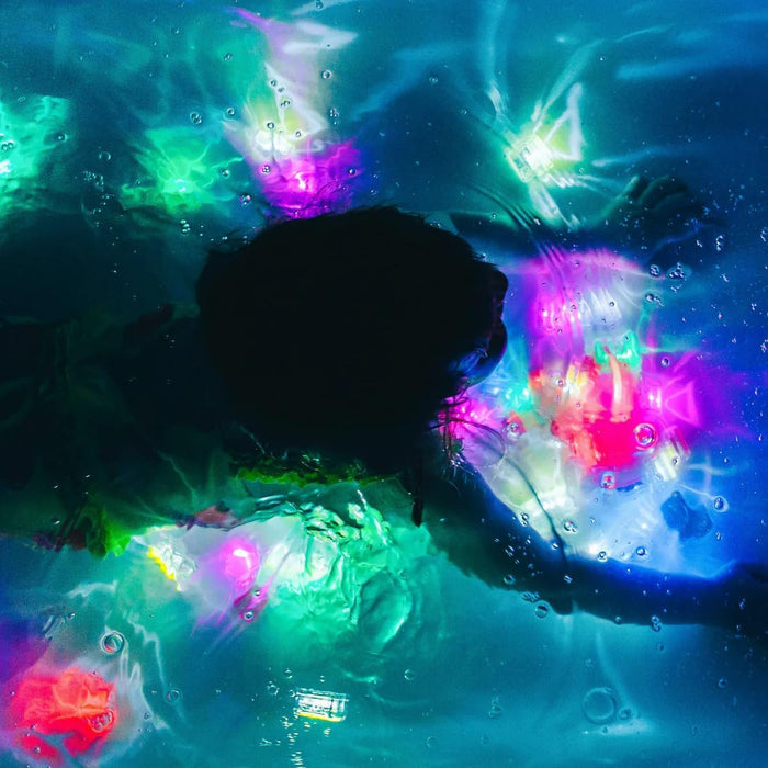 Silhouette of a child underwater with glowing pink, green, and blue light-up cubes floating in dark water.