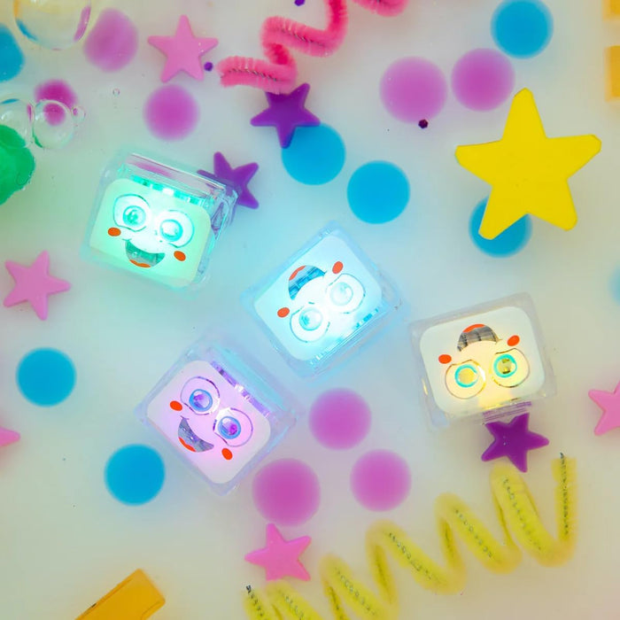 Four glowing square cubes with happy faces float in water among colorful stars, dots, and pipe cleaners.