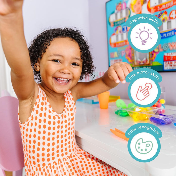 Smiling girl playing with colorful cubes and tweezers, with icons for cognitive, motor, and color recognition skills.