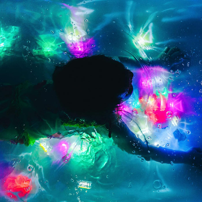 Silhouette of a person swimming underwater with glowing pink, green, and yellow cubes in dark, bubbly blue water.